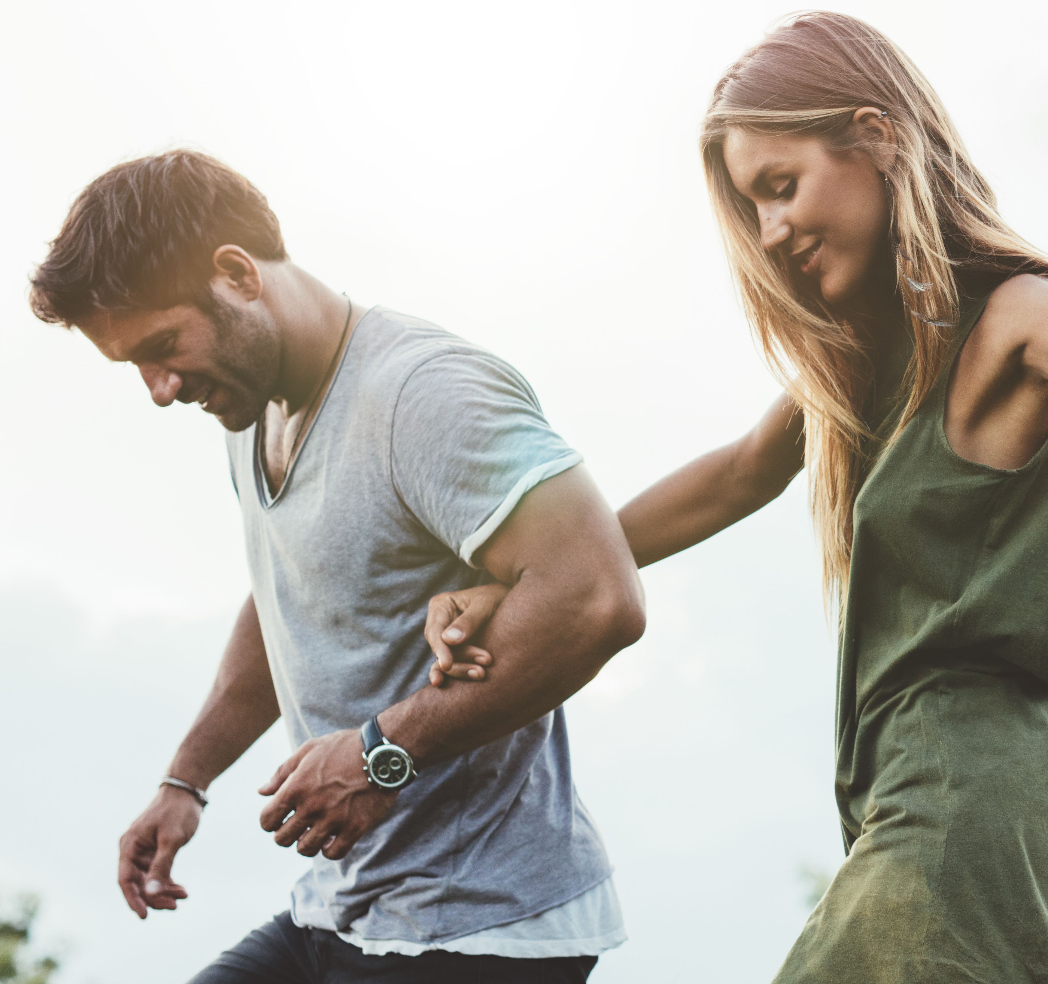 Outdoor shot of young couple walking through meadow hand in hand. Man and woman talking walk through grass field in countryside.